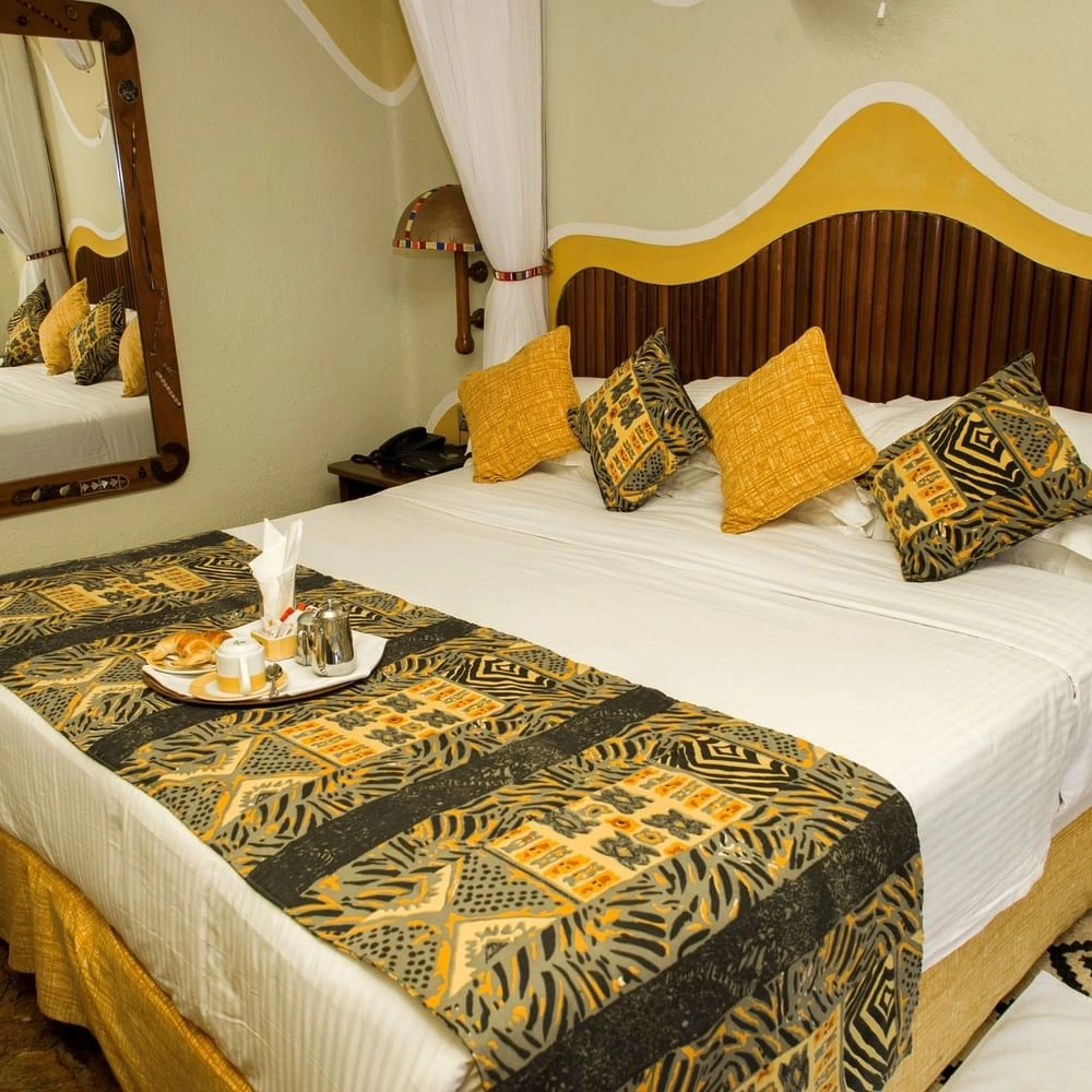 White bed on breakfast and yellow accent pillows below a wave-accented in Standard King Room at Mara Serena Safari Lodge