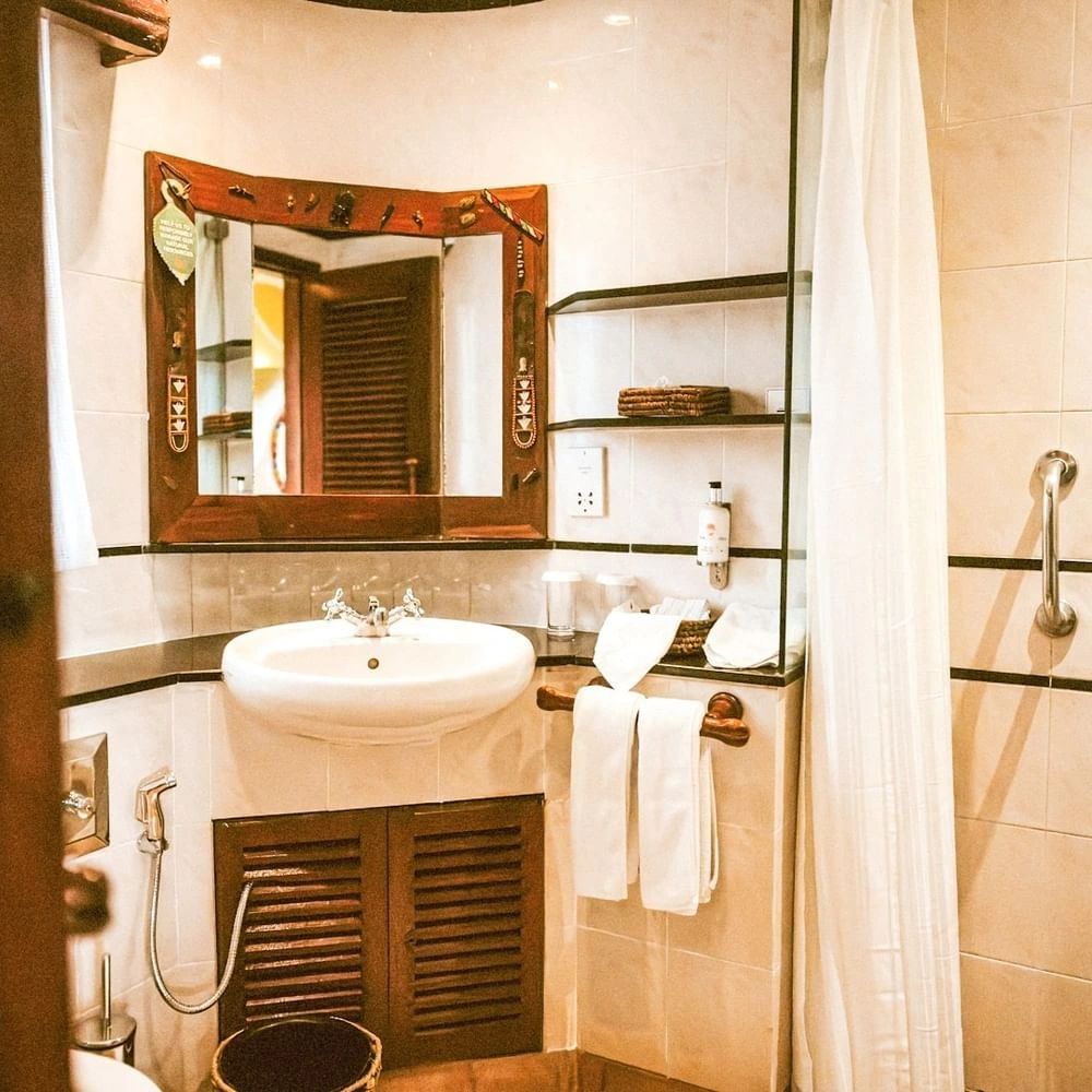 Vanity setup with sink & wood mirror frame, and a white shower curtain in Standard King Room at Mara Serena Safari Lodge