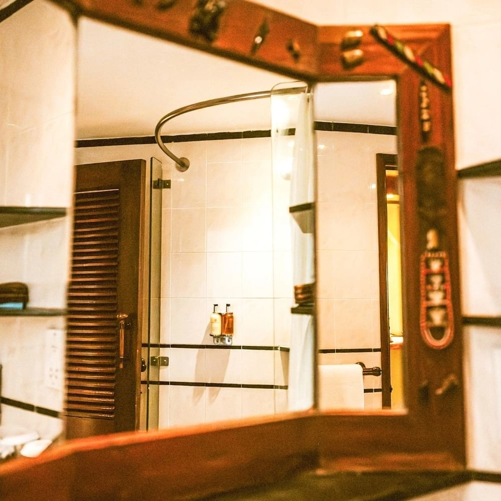 Wooden vanity mirror reflecting walk-in tile shower bathroom doorway in Standard King Room at Serena Hotels & Spa