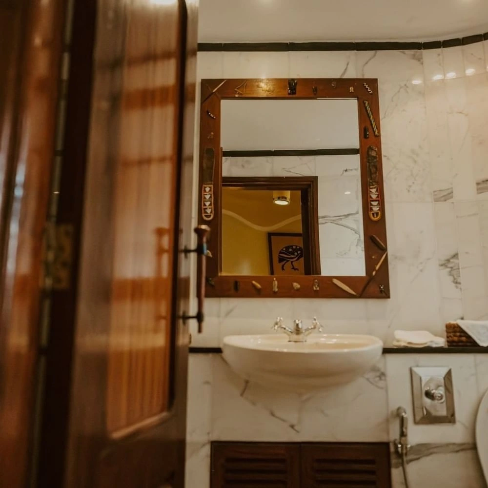 White pedestal sink under a dark wood-framed mirror decorated in Standard Twin Room at Mara Serena Safari Lodge