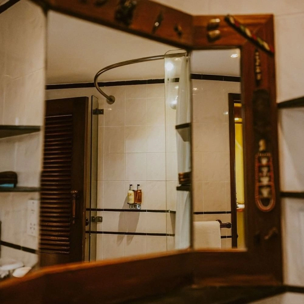 Wooden-framed mirror reflecting shower with hanging amenities and curtain in Standard Twin Room at Serena Beach Resort & Spa