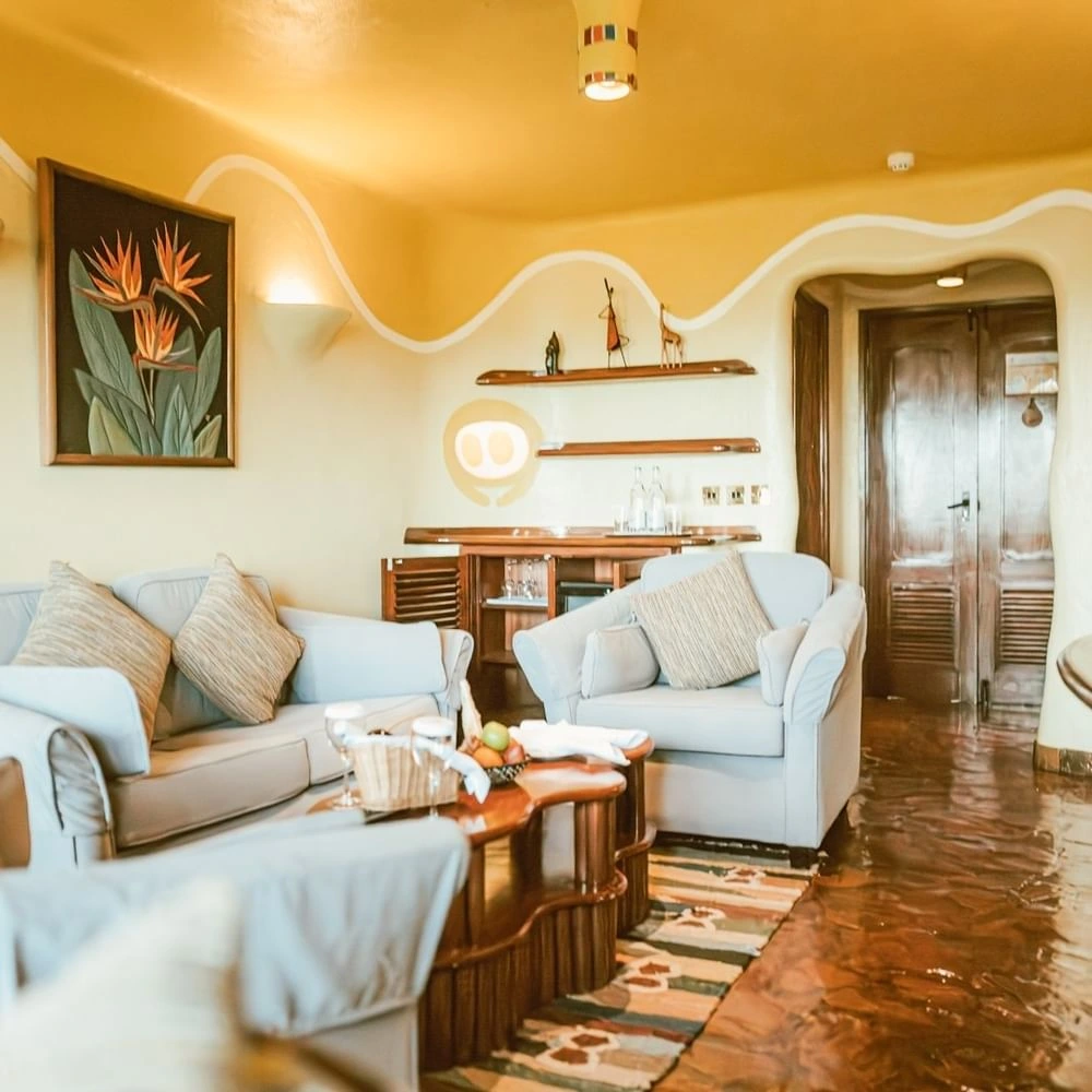 Lounge with grey sofas, and wooden floor, and a bird of paradise painting in The Suite at Mara Serena Safari Lodge