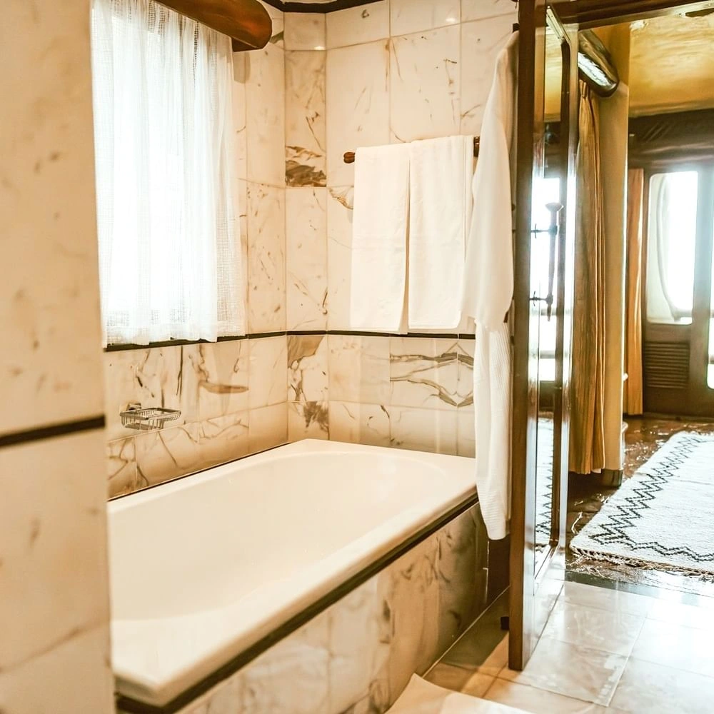 Double vanity sink with a large silver-framed mirror & scales, and a modern bathtub in The Suite at Mara Serena Safari Lodge