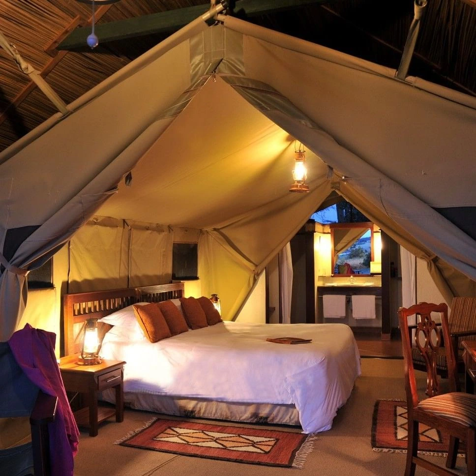 King bed lit by lanterns inside safari tent in Standard King Tent at Sweetwaters Serena Camp, capturing warm resort in Africa