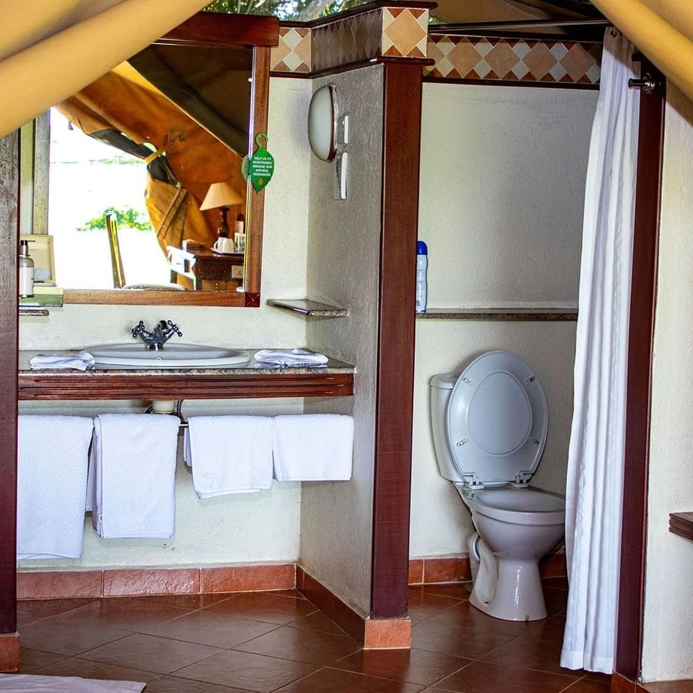 Bathroom vanity with towels hanging beside an open toilet cubicle in Standard Tent Waterhole View at Sweetwaters Serena Camp