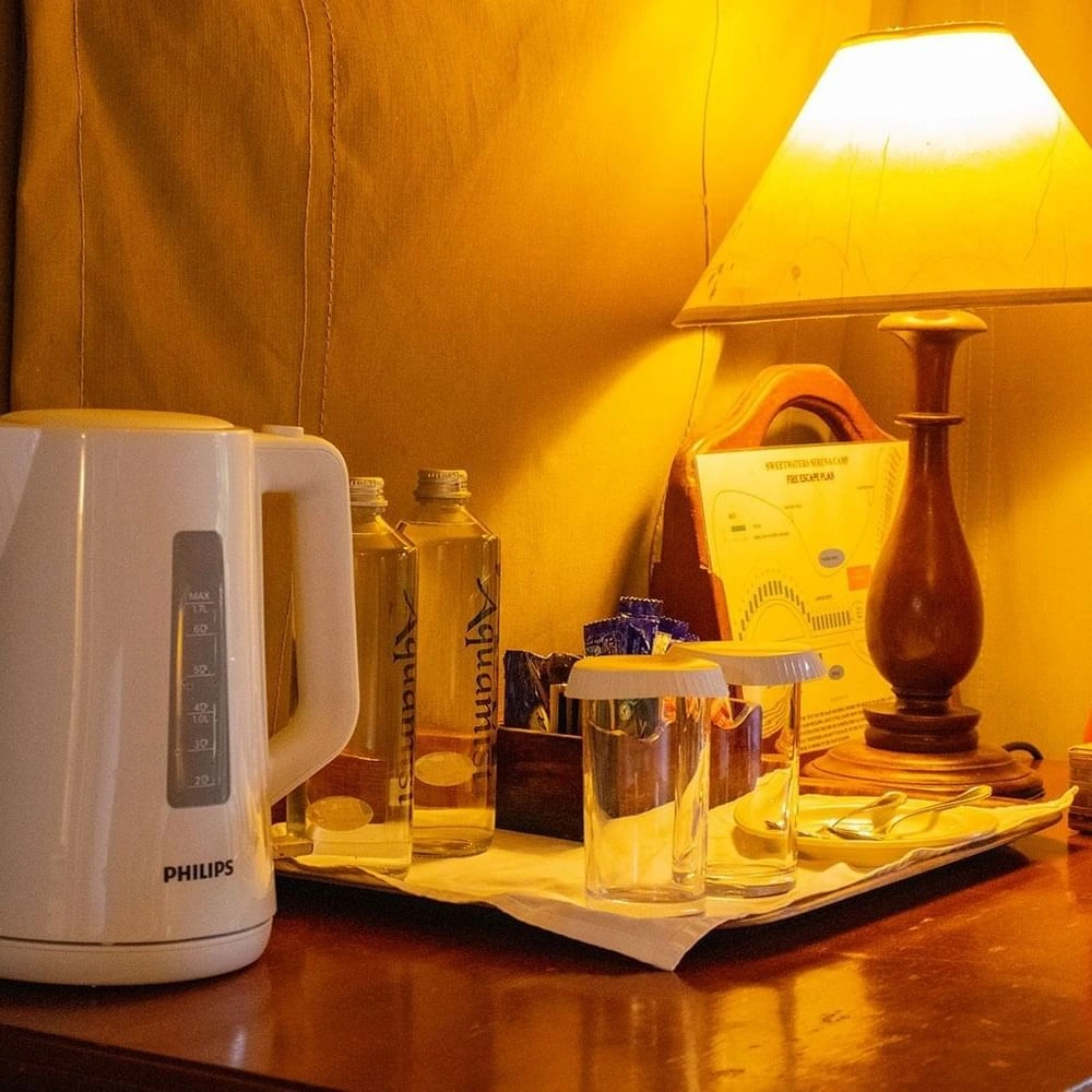 Electric kettle alongside bottled water and wooden table lamp on a desk in Standard Twin Room at Serena Beach Resort & Spa