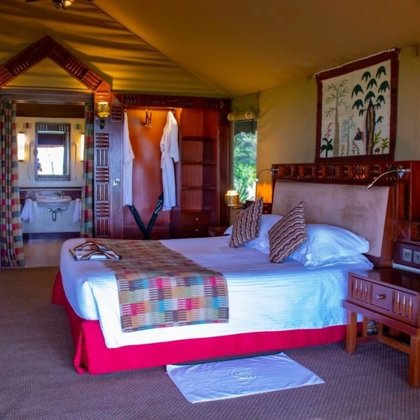 Large bed by a wooden nightstand surrounding a view of an open bathroom area in Morani Deluxe Tent at Sweetwaters Serena Camp